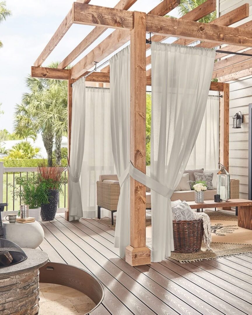 A patio with a wooden deck and white curtains.